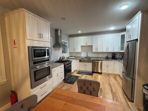 A modern kitchen with stainless steel appliances, white cabinetry, and a wooden dining table.
