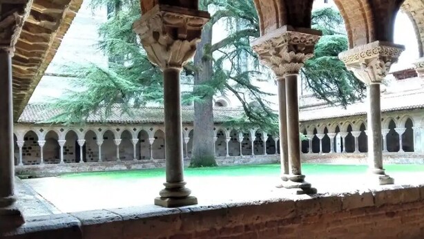 Une cour bordée de colonnes et d’arcs en pierre, entourée d’arbres et d’un bâtiment doté d’un toit en tuiles.
