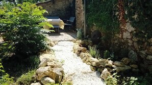 Un chemin de pierres mène à un espace de détente extérieur rustique, agrémenté d’une table et de chaises.