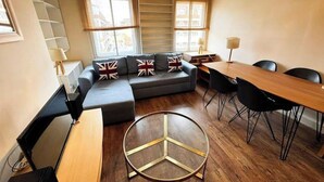 Un salon moderne avec un canapé d’angle, une table basse ronde et un coin repas comprenant une table et des chaises en bois.