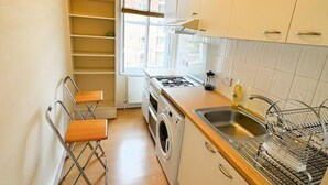 Une cuisine compacte équipée d’un lave-linge encastré, d’un évier et d’une fenêtre laissant entrer la lumière naturelle.