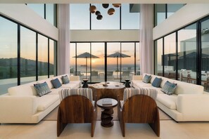 Un salon moderne doté d’une grande fenêtre, de deux canapés, d’une table basse et offrant une vue sur le coucher de soleil.