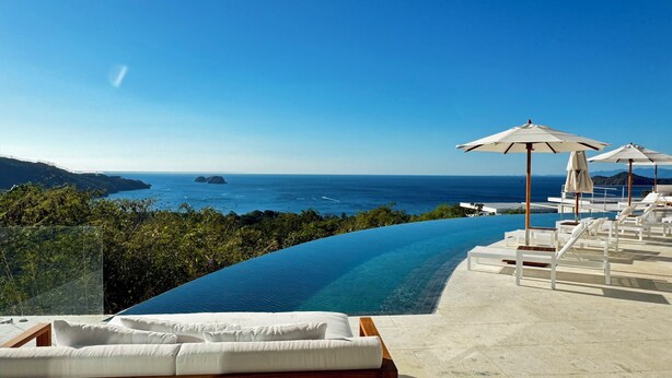 A infinity pool with a view of the ocean and mountains, lounge chairs, and umbrellas. - Villa Solea - Stunning New Luxury 6-bedroom villa in beautiful Playa Hermosa (Playa Hermosa)