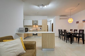 A modern kitchen with white cabinets, a central island, and a dining area with a table and chairs. - Ortigia Collection / Suite No.1 / Terrace (Swieqi)