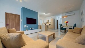 A modern living room with a TV, sofa, coffee table, and a dining area with chairs and a table. - Ortigia Collection / Suite No.1 / Terrace (Swieqi)