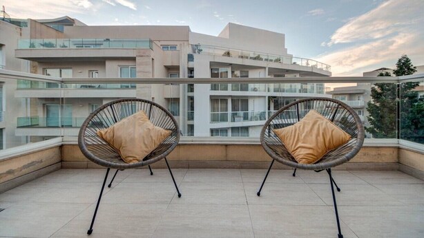 A balcony with two wicker chairs and cushions, overlooking a modern apartment building. - Ortigia Collection / Suite No.4 / Terrace (Swieqi)
