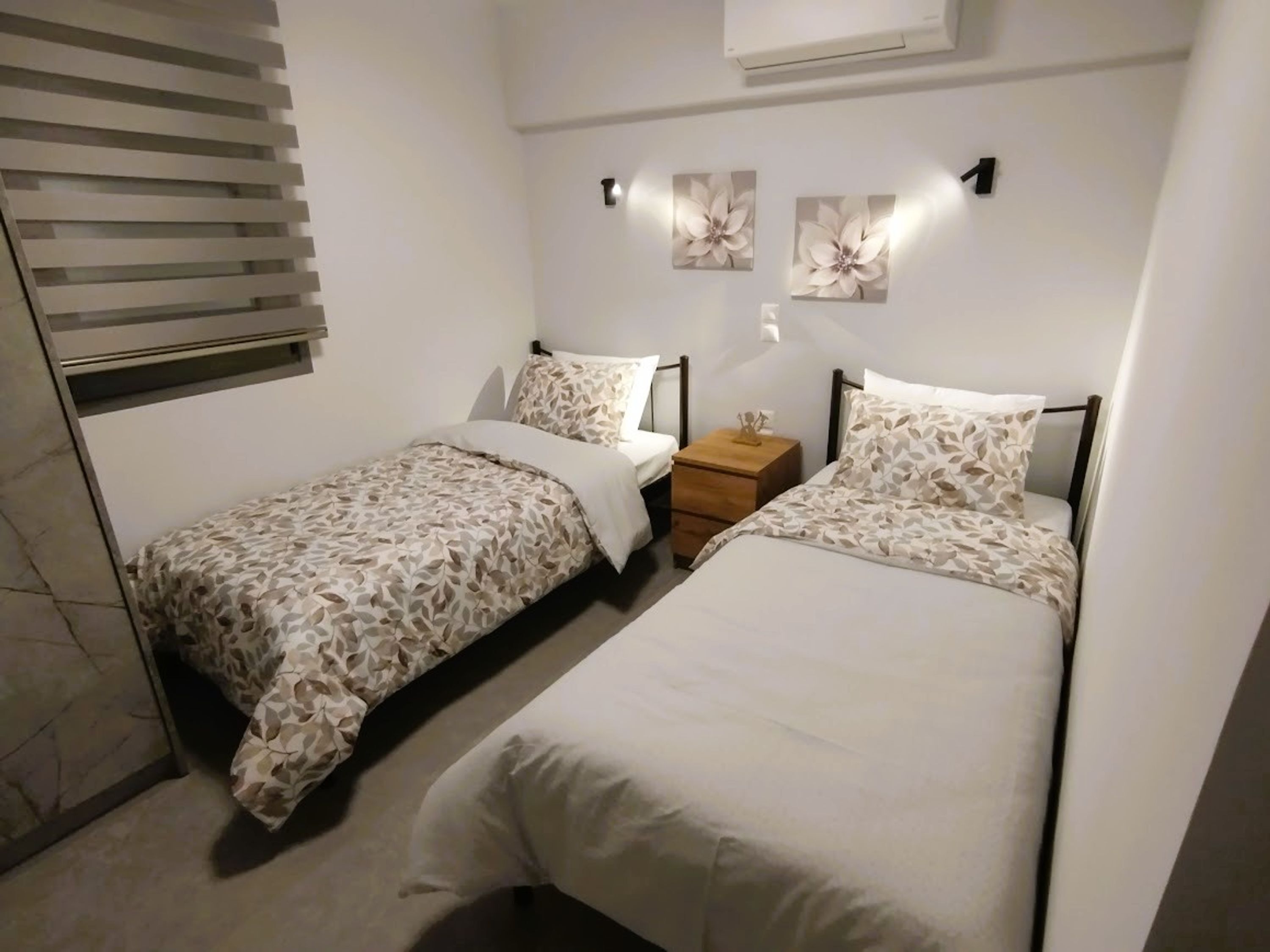 A bedroom with two single beds, a nightstand, and a wall-mounted air conditioner.
