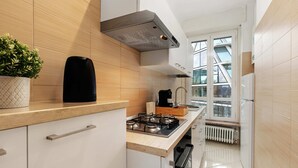 Une cuisine moderne avec des meubles blancs, une cuisinière à gaz, une machine à café et une fenêtre donnant sur l’extérieur.