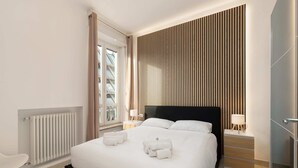 Une chambre d’hôtel moderne avec un grand lit, un mur recouvert de lambris en bois, une fenêtre avec des rideaux, un radiateur et une table de chevet avec une lampe.