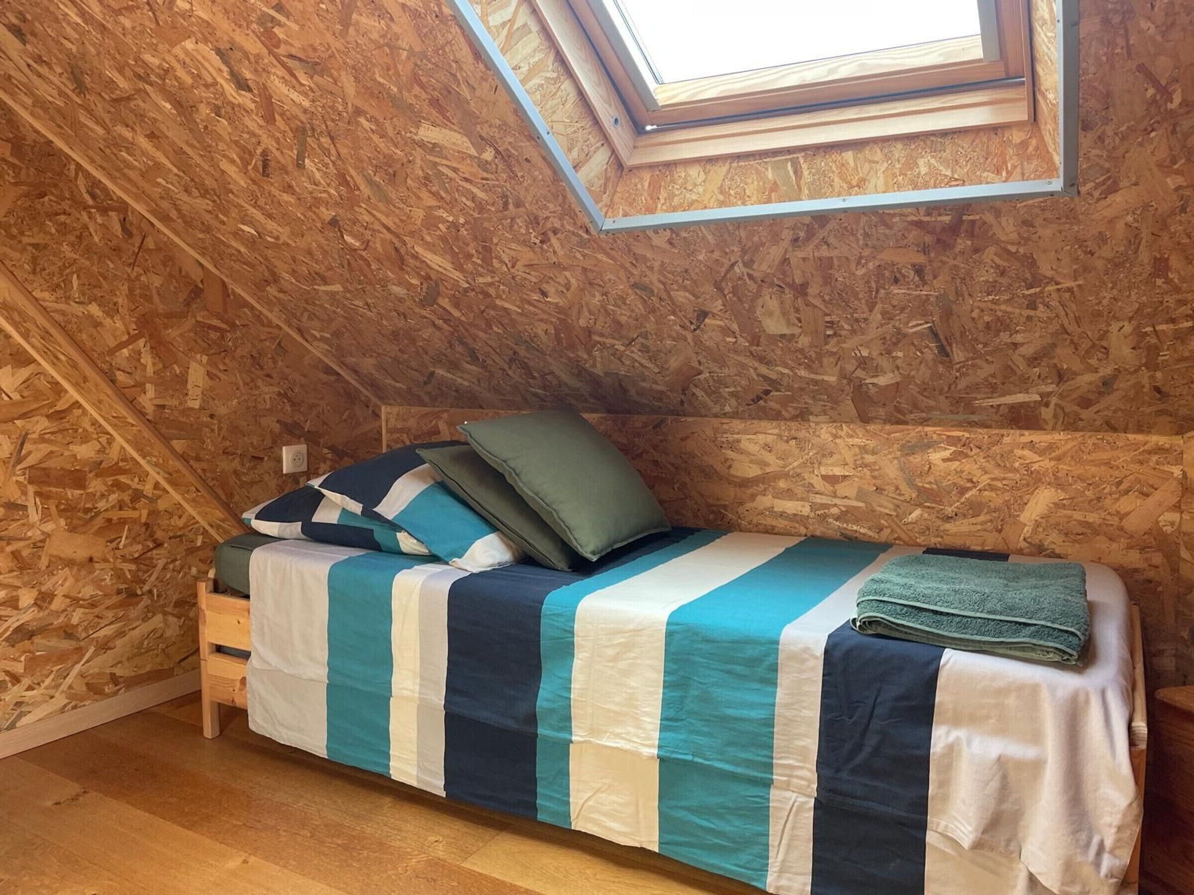A small, single-bed room with a sloped ceiling and wooden walls.