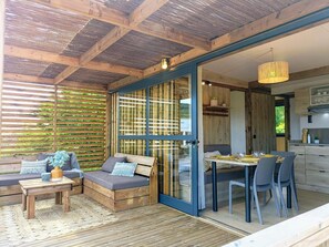 A cozy outdoor seating area with a sofa and table, a dining table with chairs, and a kitchen visible through glass doors. - Scenic cabin with wifi, pets allowed, parking (Bioussac)