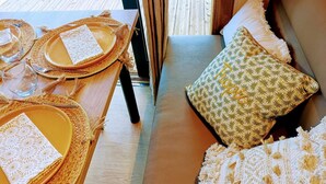 Una habitación acogedora con una terraza de madera, un sofá con cojines estampados y una mesa de comedor con individuales tejidos y cubiertos.