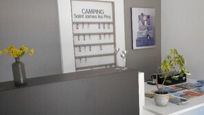 En receptionsdisk med en skylt med texten ”CAMPING Saint James les Pins”, en vas med gula blommor och en krukväxt.