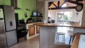 Uma cozinha com fogão embutido, micro-ondas e frigorífico. Há uma ilha de madeira com bancos e um relógio na parede.