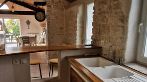 Cozinha com paredes de pedra, bancada de madeira, pia e janela.