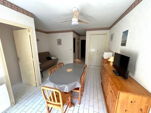 A dining area with a table, chairs, a ceiling fan, a television, and a cabinet. - Argelès: Apartment for 4 near beach, private parking (Argelès-sur-Mer)