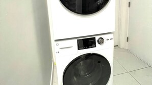 A stacked washer and dryer unit in a hallway with white walls and a tiled floor.