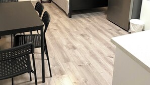 Habitación compacta con cama, una mesa de comedor con sillas, refrigerador y una mesita de noche con lámpara.