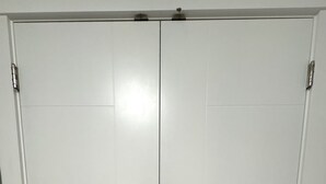 A set of double doors with a simple, functional design, featuring two handles and a central locking mechanism.