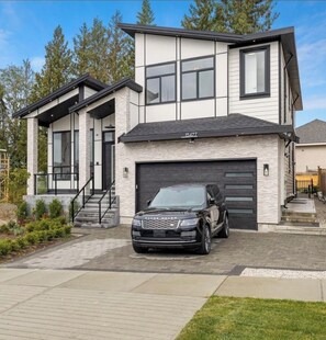 Una casa moderna a due piani con garage, vialetto e una Range Rover nera parcheggiata davanti.