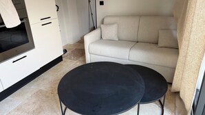 Una cocina moderna con horno empotrado, un sofá beige y dos mesas negras.