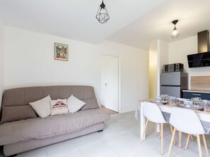A modern living room with a sofa, dining table, chairs, and a kitchen area with appliances. - Cozy apartment with terrace and WIFI in Saint-Lary (Saint-Lary-Soulan)