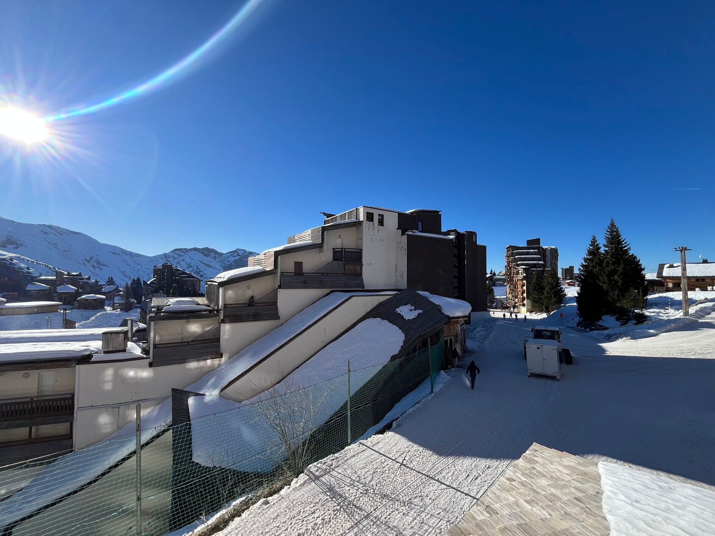 Eine verschneite Landschaft mit Gebäuden, einer Skipiste und Bergen im Hintergrund.