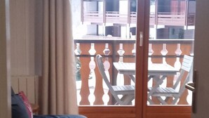 Une pièce dotée d’une porte en bois qui donne sur un balcon extérieur, où se trouvent des chaises et des tables blanches.