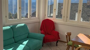Una habitación con un sofá color turquesa, una silla roja, una mesa de madera y vistas a montañas a través de amplias ventanas.