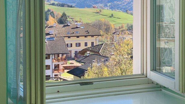 Una ventana con vistas a un pueblo, montañas y un cielo despejado.