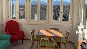 Un comedor con mesa y sillas de madera, una silla roja, un sofá verde y ventanas grandes con vista a las montañas.