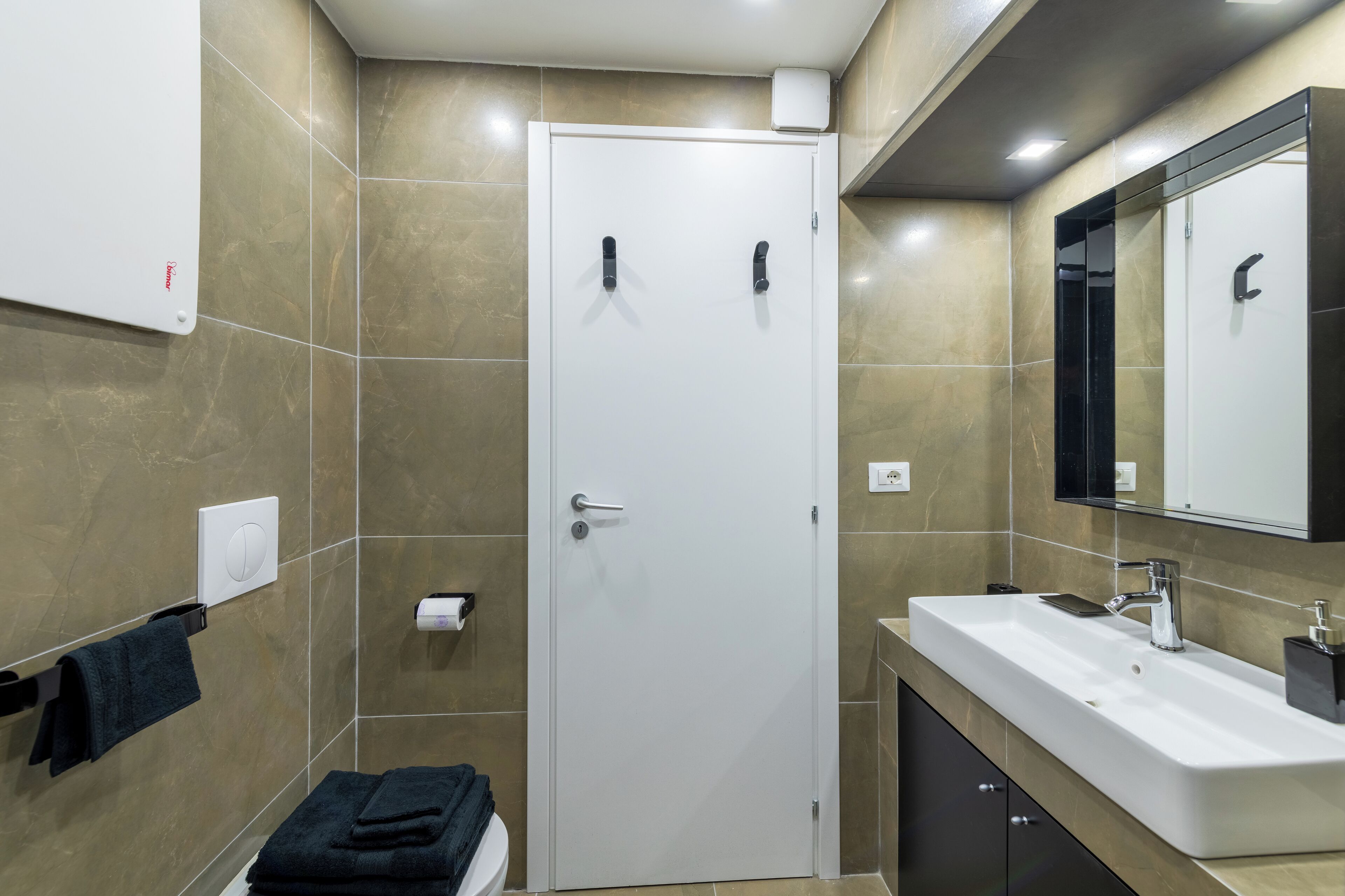 A modern bathroom with a white door, a sink with a mirror, and a towel rack.