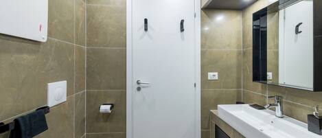 A modern bathroom with a white door, a sink with a mirror, and a towel rack.