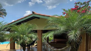 Un espacio al aire libre techado con una hamaca, palmeras y un edificio de ladrillo.