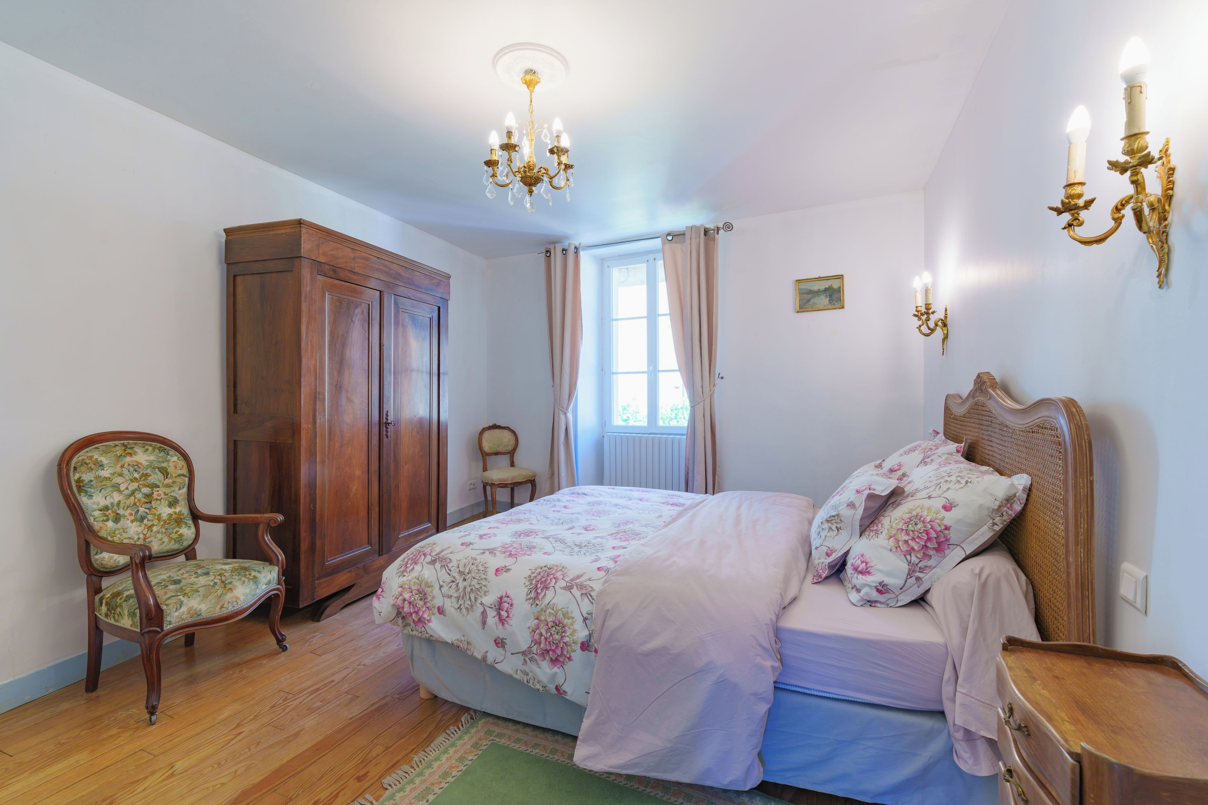 A bedroom with a bed, a wooden wardrobe, a chair, and a window with curtains.