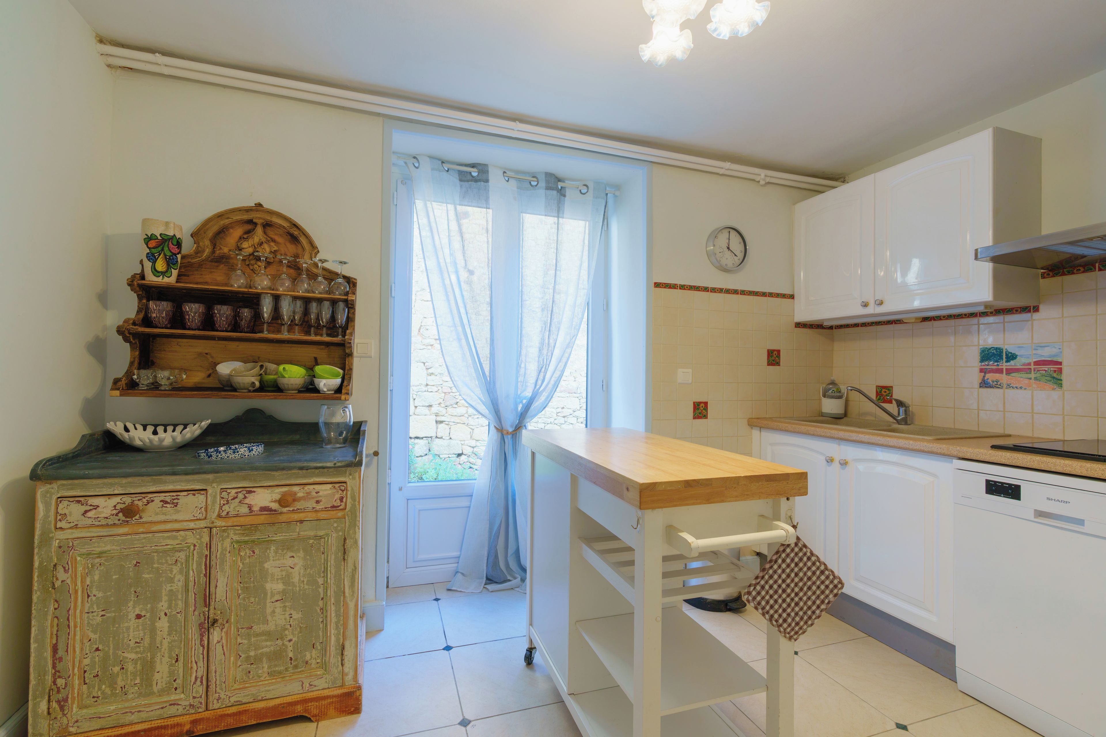 A kitchen with a wooden cabinet, a window with a curtain, and a clock on the wall.