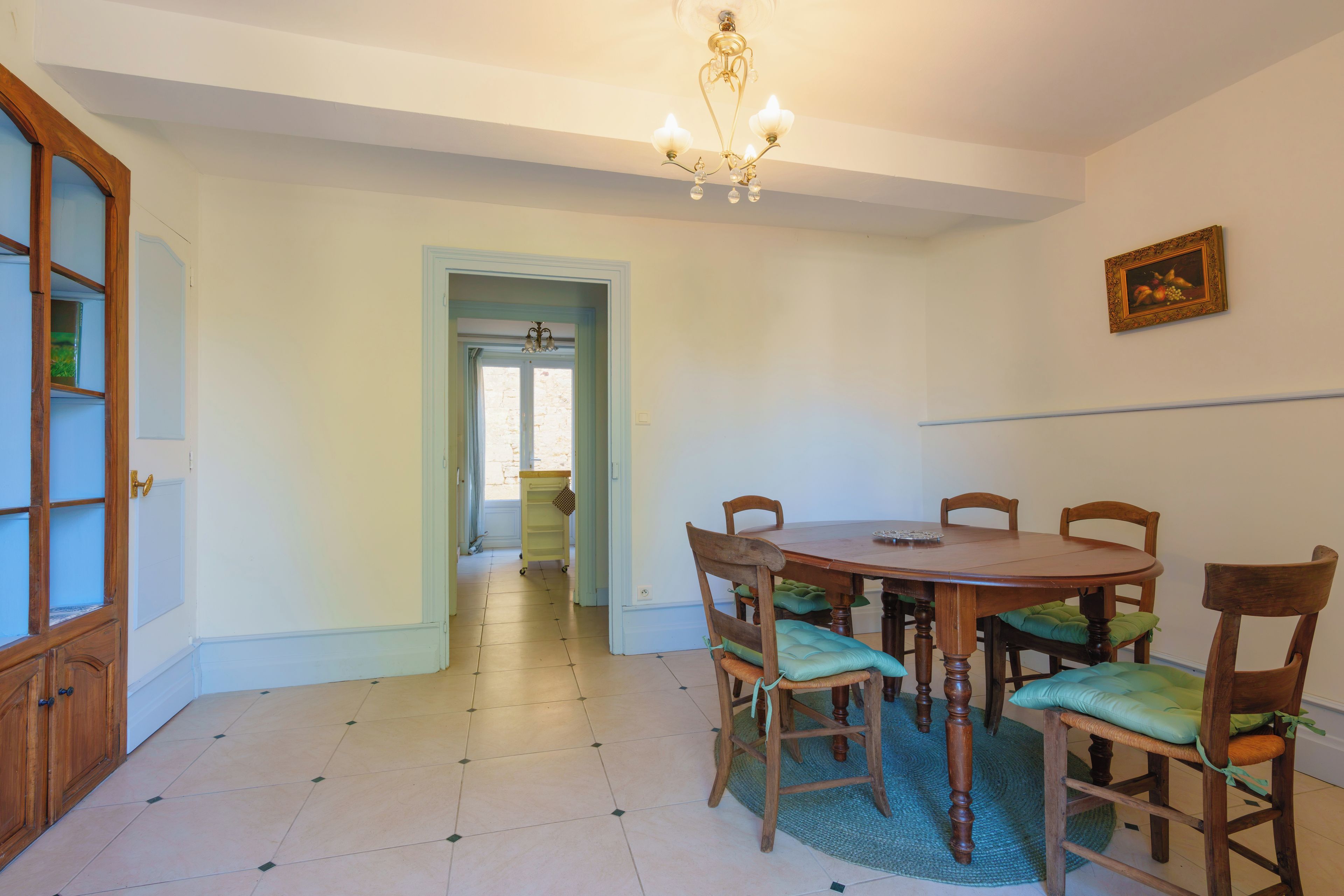 Un comedor con mesa y sillas de madera, una araña y una puerta que da a otra habitación.