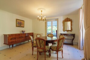 A dining room with a wooden table, six chairs, a chandelier, a painting, a mirror, and a window with a view. - Maison Marius—pets allowed—1,600 m² fenced-in garden—heated pool (Le Buisson-de-Cadouin)