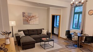 Ein modernes Wohnzimmer mit einem Ecksofa, einem Couchtisch und einer Essecke mit Stühlen und einem Tisch für zwei Personen.