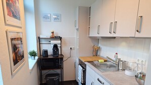 Eine kompakte Küche mit Mikrowelle, Toaster und Kaffeemaschine auf einer Ablage, einem Spülbecken mit Wasserkocher und einem Mülleimer.