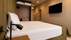 Una habitación de hotel con cama, escritorio con lámpara, televisor en la pared y armario.
