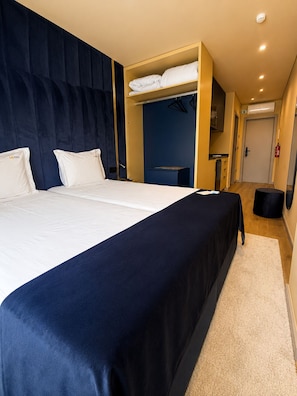 A hotel room with a large bed, a wardrobe, a desk, and a small stool.