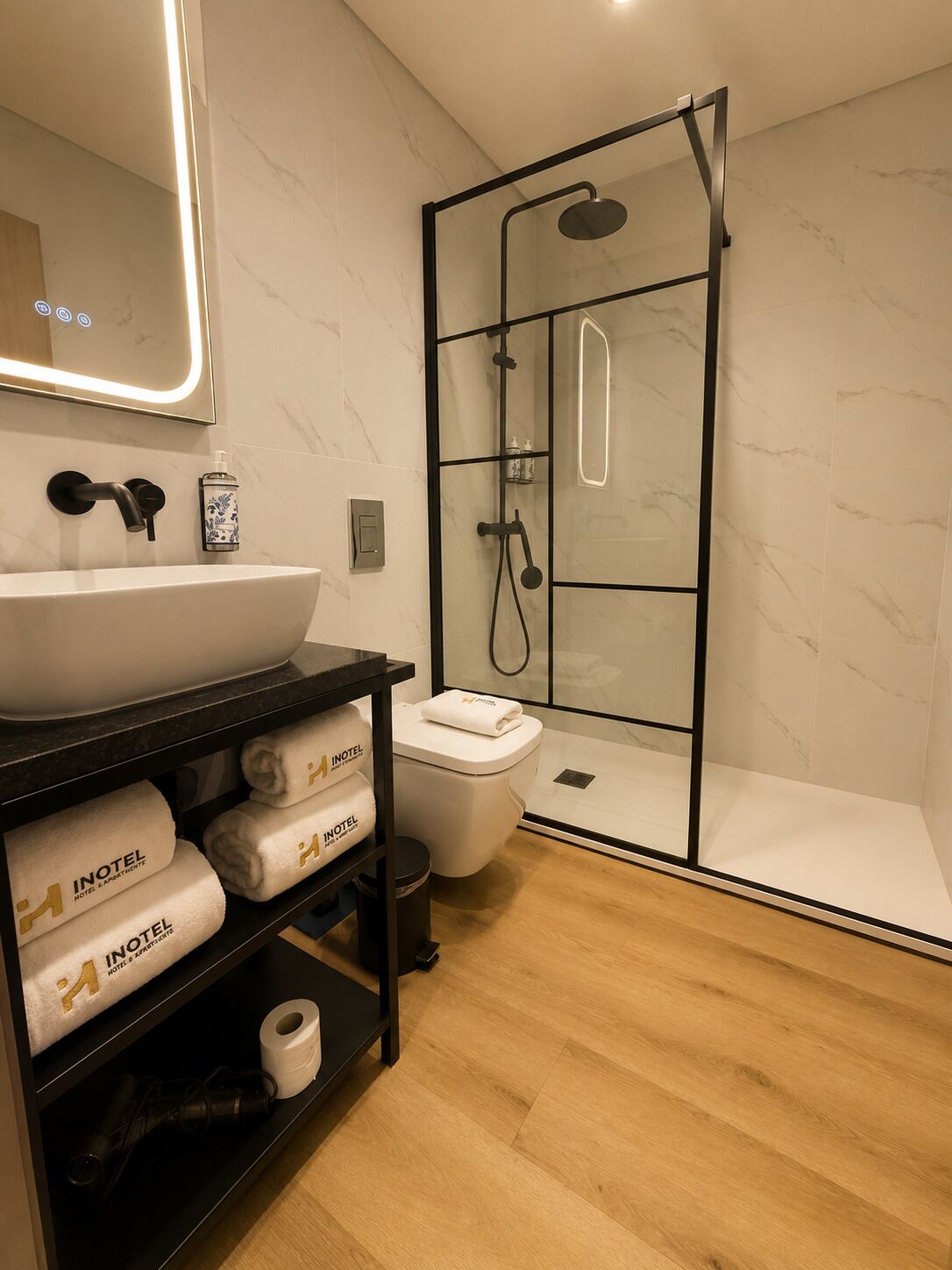 A modern bathroom with a glass-enclosed shower, a white sink, and a black vanity with towels.