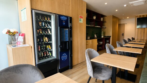 Un interior de restaurante con mesas y sillas de madera, una máquina expendedora y una barra con un menú.