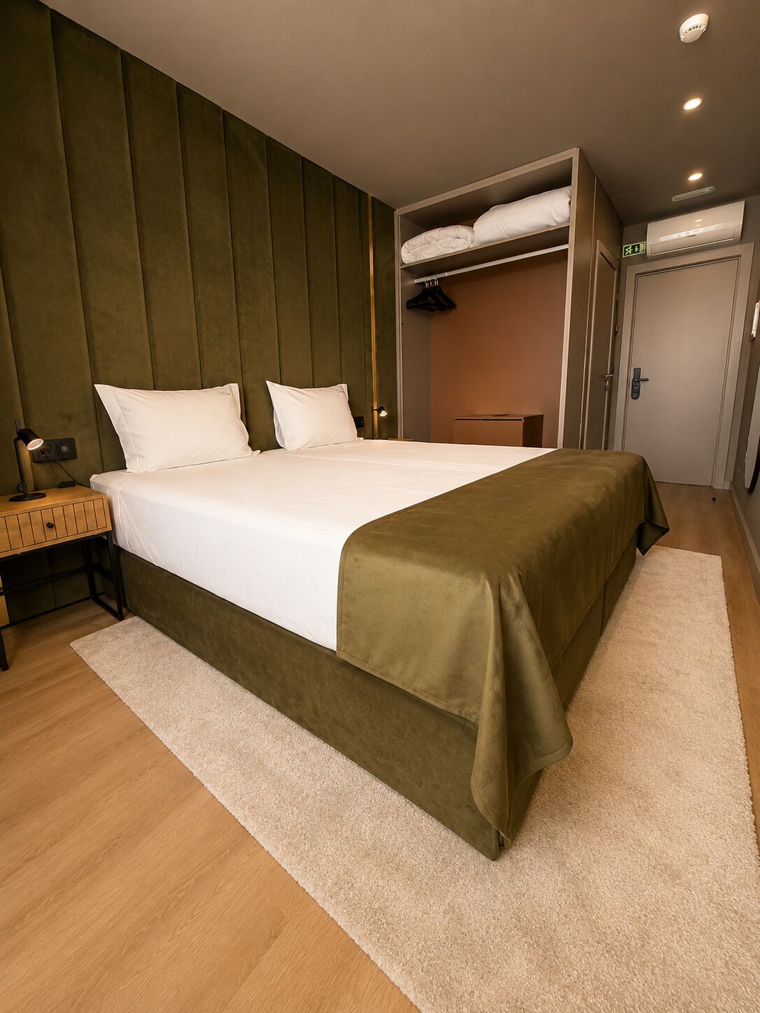 Une chambre d’hôtel bien rangée, avec un lit, une table de chevet, une lampe, une armoire et une porte.