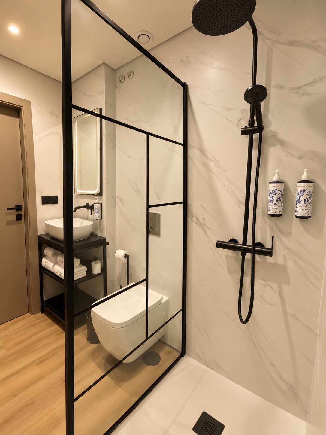 Un baño moderno con ducha envuelta en vidrio, un lavamanos blanco y pared revestida de mármol.