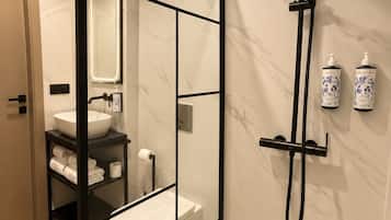 Un baño moderno con ducha envuelta en vidrio, un lavamanos blanco y pared revestida de mármol.