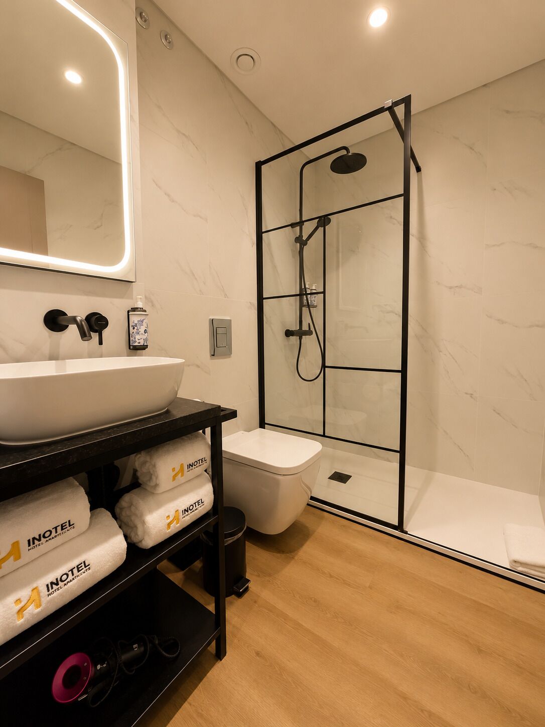 A modern bathroom with a glass-enclosed shower, a white sink, and a shelf with folded towels.