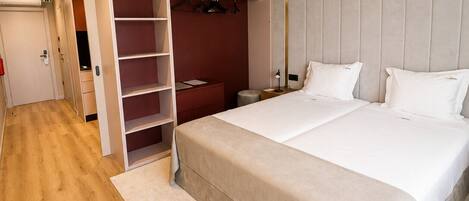 A modern hotel room with a large bed, a wardrobe with hanging space, a bedside table, and a small stool.