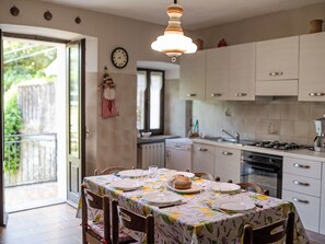 Un'area pranzo con tavolo imbandito per quattro, una cucina sullo sfondo e vista all'esterno.